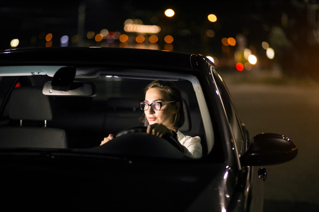 Carro com faróis iluminando estrada escura à noite, realçando a importância da iluminação adequada para Direção Noturna Segura.